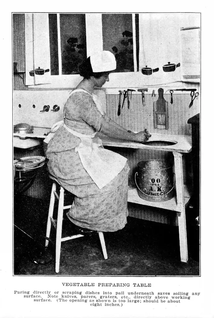 Vintage photo of a woman preparing vegetables at a kitchen work table with tools hanging above, 1919