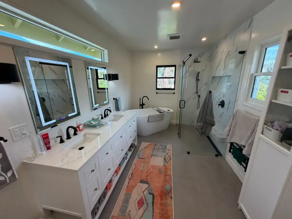 Bathroom remodel with a freestanding soaking tub, glass-enclosed walk-in shower with marble-look tile, and a handheld shower on a vertical slide bar.