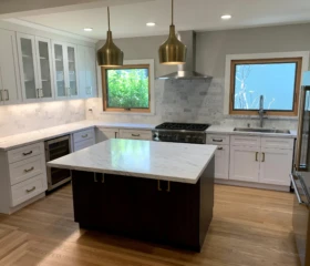 Elegant finishes and contrasting cabinetry create a sophisticated kitchen design. Moraga Luxury kitchen with white shaker cabinets, dark wood island, marble backsplash, brass pendant lights, and wine refrigerator.