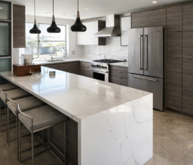 A spacious kitchen designed around a large waterfall island for cooking, dining, and entertaining. San Francisco Luxury kitchen remodel with oversized quartz waterfall island, dark wood cabinetry, pendant lighting, and stainless steel appliances.