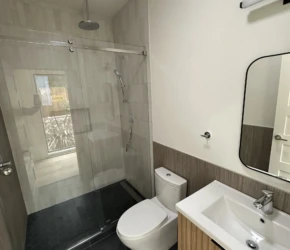 A modern Berkeley ADU bathroom featuring a frameless glass shower, custom wood vanity, black tile flooring, and clean contemporary finishes. Modern Berkeley ADU bathroom featuring a frameless glass walk-in shower, black hexagon floor tile, light wood floating vanity, large-format wall tile, and a minimalist contemporary design.