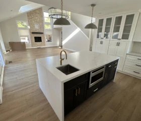 A bright open-concept kitchen designed for modern family living. Walnut Creek Open-concept kitchen with white cabinetry, black island, waterfall quartz countertops, and adjacent living room.