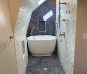 A custom San Francisco bathroom remodel transforming an attic space into a luxurious spa-inspired retreat with a freestanding tub, walk-in shower, and premium finishes. Luxury attic bathroom remodel in San Francisco featuring a freestanding soaking tub, walk-in shower, white penny tile walls, dark mosaic floor tile, brushed brass fixtures, and a vaulted ceiling with skylight.