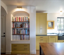 Arched built-in bookcase beside custom kitchen cabinetry. Berkeley Arched built-in bookcase beside custom yellow kitchen cabinets and farmhouse sink.