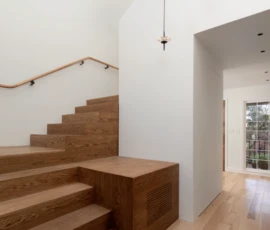 Sculptural pendant lights over a custom wood staircase. Remodeled stairwell with oak stairs, curved wood handrail, and pendant lights.