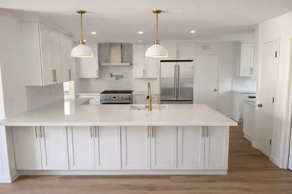 Luxury white shaker kitchen featuring a waterfall quartz island, brass pendant lighting, stainless steel range, pot filler, and custom cabinetry in an East Bay home.