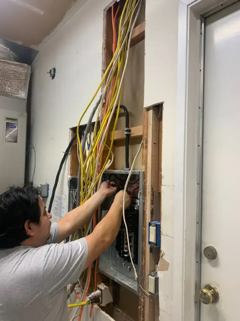 Electrician wiring a new panel with the wall opened and new branch circuit cables run down into the enclosure