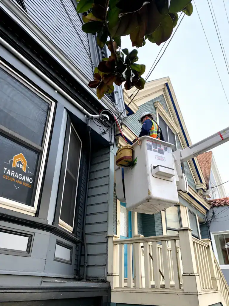Utility crew in a bucket lift working on the overhead electrical service at the roofline of a San Francisco home