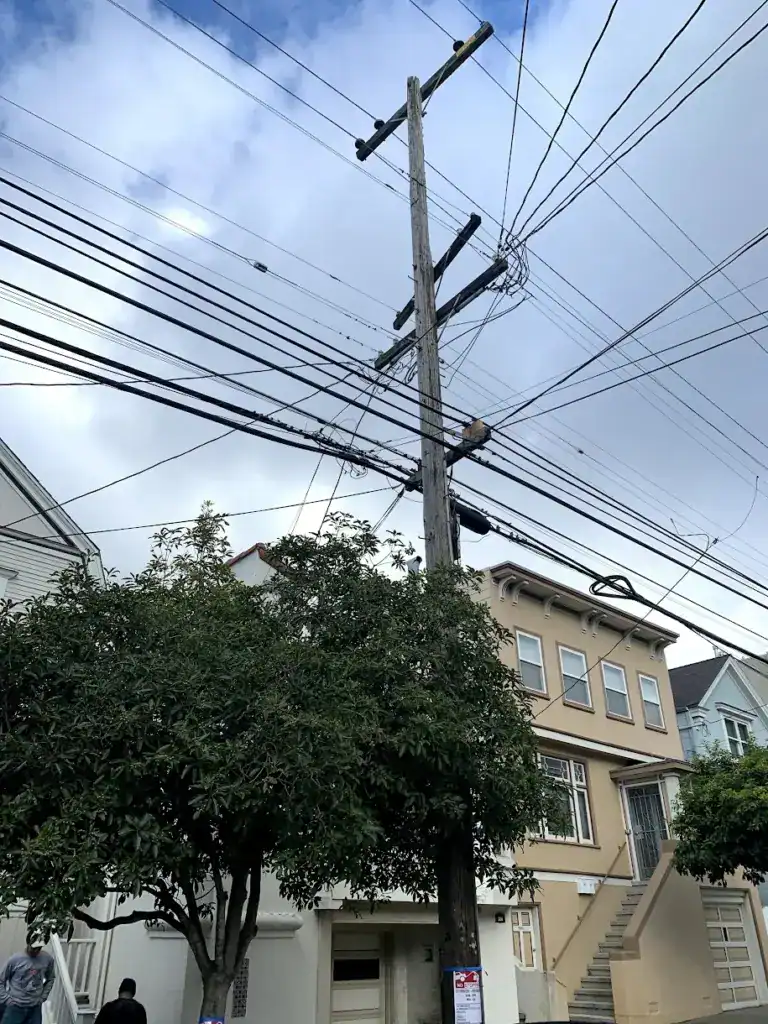 Utility pole crowded with overhead conductors and service drops on a San Francisco street of wall-to-wall homes